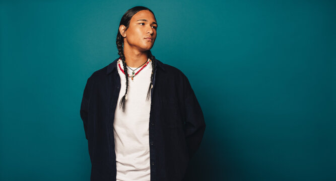 Native American man with braided hair and cultural jewelry standing in a studio