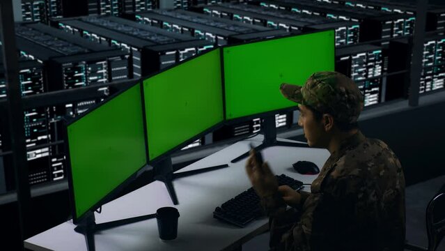 Side View Of Asian Military Talking On Mobile Phone While Working With Mock Up Multiple Computer Monitor In Data Center