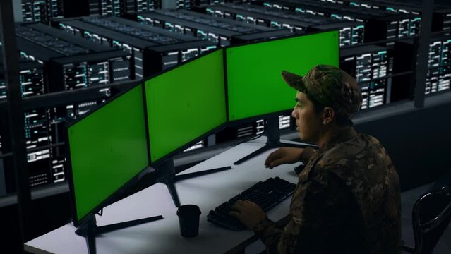 Side View Of Bored Asian Military Working With Mock Up Multiple Computer Monitor In Data Center