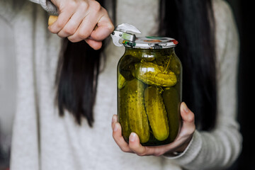 An adult woman, a gardener, a cook, holds in her hands in the kitchen a glass jar of vegetables...