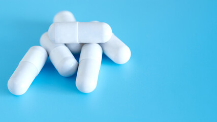 White medicine capsules on a blue background, close up.