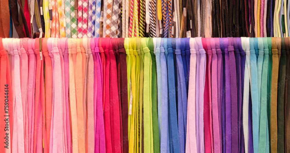 Leinwandbilder A row of colorful strings laces are displayed in a store. The colors are bright and vibrant, creating a cheerful and lively atmosphere. The strings are arranged in a way that showcases their variety
