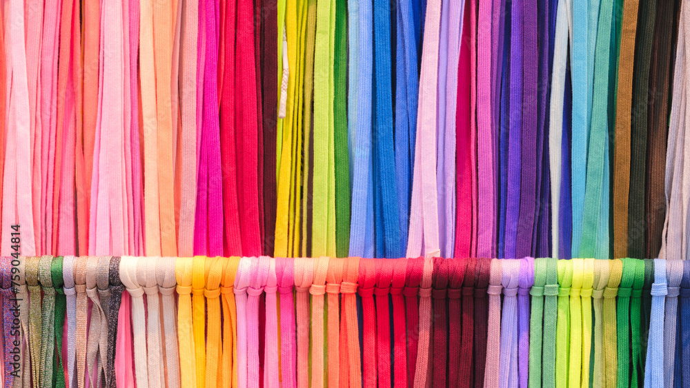 Fototapete a row of colorful strings laces are displayed in a store. the colors are bright and vibrant, creatin