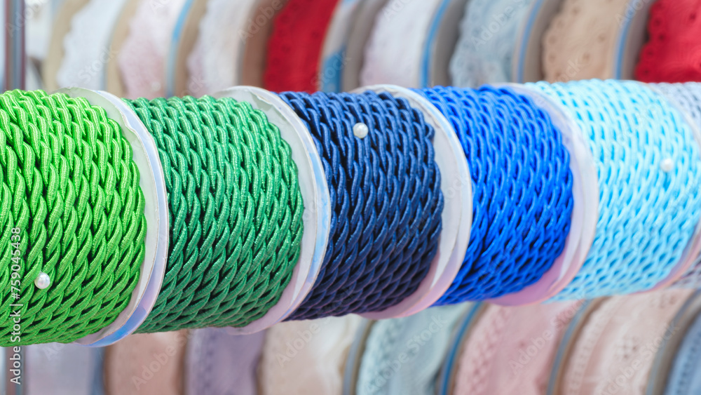Aufkleber A row of colorful spools of thread, tape, braid  are displayed in a store. The spools are arranged in a rainbow pattern, with each color being represented in the display. The spools various sizes