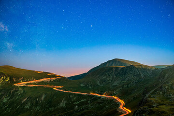 Transalpina road under a starry night with traffic trails along the winding road. Transalpina is one of the highest roads passing the Carpathians in Romania. - 759046489