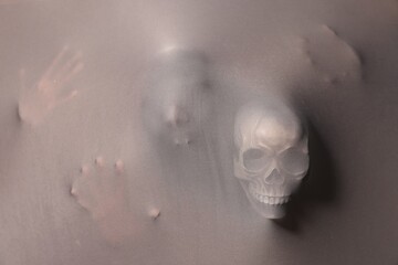 Silhouette of creepy ghost with skulls behind grey cloth