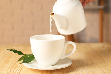 Pouring tasty tea into cup at light wooden table, closeup