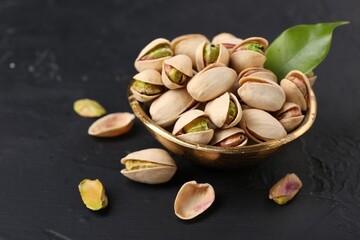 Tasty pistachios in bowl on black table, closeup. Space for text