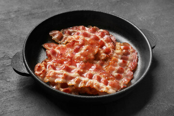 Fried bacon slices on dark textured table, closeup
