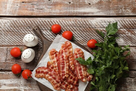 Fried bacon slices, tomatoes, parsley and spices on wooden rustic table, flat lay