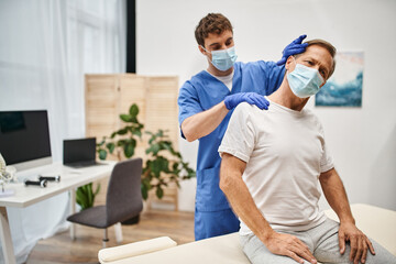 good looking dedicated doctor with mask and gloves stretching his mature patient on rehabilitation
