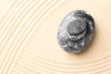 Zen garden stones on beige sand with pattern, top view. Space for text