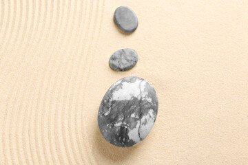 Zen garden stones on beige sand with pattern, flat lay