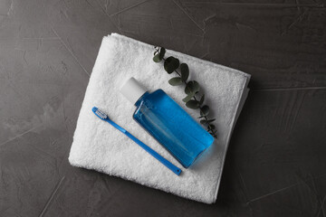 Fresh mouthwash in bottle, toothbrush, eucalyptus branch and towel on dark textured table, top view
