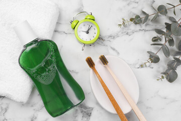 Fototapeta na wymiar Fresh mouthwash in bottle, toothbrushes and alarm clock on white marble table, flat lay