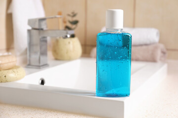 Fresh mouthwash in bottle on sink in bathroom, closeup. Space for text