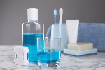 Fototapeta na wymiar Fresh mouthwash in bottle, glass and dental floss on white marble table, closeup