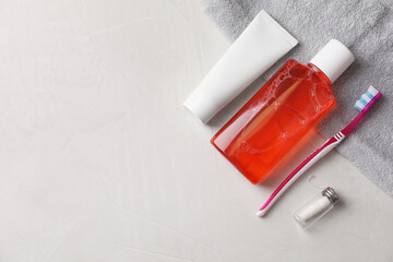 Fresh mouthwash in bottle, toothpaste, toothbrush and dental floss on light textured background,...