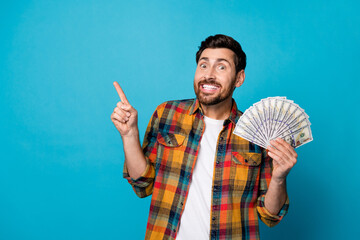 Photo of excited man with beard dressed stylish plaid shirt hold dollars indicating at sale empty space isolated on blue color background - obrazy, fototapety, plakaty