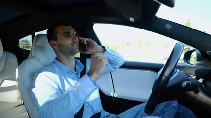 Male entrepreneur speaking by smartphone during riding on electrical auto with autopilot at urban road. Confident businessman talking on phone while riding an autonomous self driving electric car