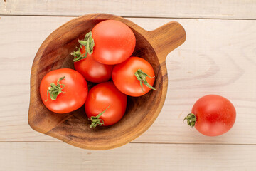 Several cocktail tomatoes in a wooden cup on a wooden table, macro, top view.
