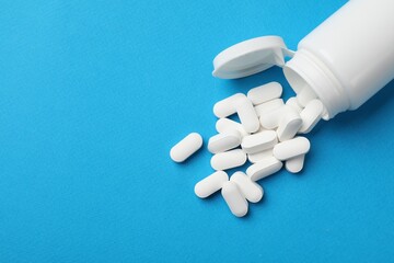 Vitamin pills and bottle on light blue background, top view. Space for text