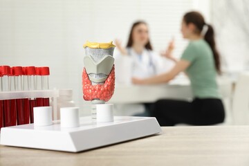 Endocrinologist examining patient at clinic, focus on model of thyroid gland and blood samples in...