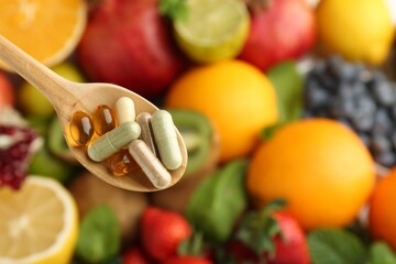 Different vitamin pills in spoon over fresh fruits, top view. Space for text