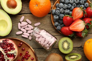 Vitamin pills in bottle and fresh fruits on wooden table, flat lay