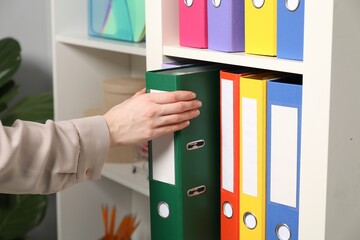 Woman taking binder office folder from shelving unit indoors, closeup
