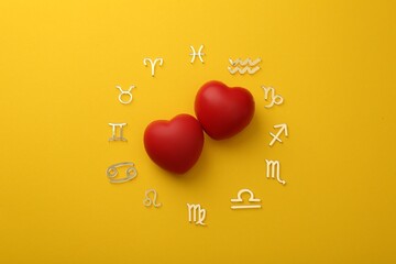 Zodiac signs and red hearts on yellow background, flat lay