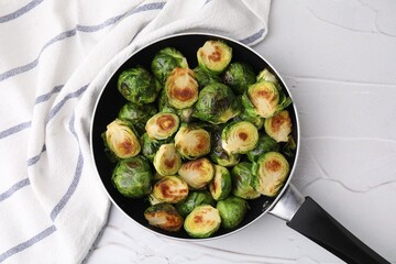 Delicious roasted Brussels sprouts in frying pan on white textured table, top view
