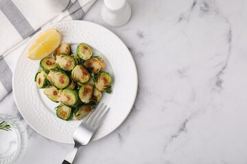 Delicious roasted Brussels sprouts, slice of lemon and fork on white marble table, top view. Space for text