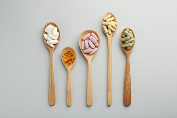 Different vitamin pills in spoons on light grey background, flat lay. Health supplement