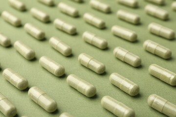 Many vitamin capsules on olive background, closeup