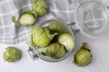 Fresh green tomatillos with husk in glass jar on light table, flat lay