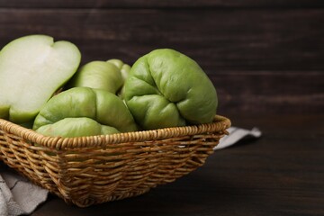 Cut and whole chayote in wicker basket on wooden table, closeup