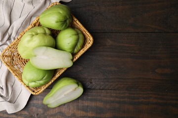 Cut and whole chayote in wicker basket on wooden table, flat lay. Space for text