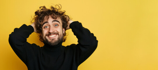 man with a beard and tousled hair is making a playful gesture to his head with his fingers, wearing a black turtleneck sweater with a joyful expression against a yellow background