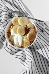 Serving Breakfast. Bowl of Greek Yogurt, Cottage Cheese, Granola, Banana Slices, on Kitchen Towel with Spoons.