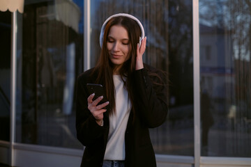 Fototapeta premium A woman in a suit and headphones dances cheerfully on the street, singing along to music, embodying joy and positivity. A freelancer enjoys the freedom of flexible work hours.