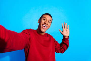 Portrait of cheerful young man toothy smile arm palm waving hi make selfie isolated on blue color...