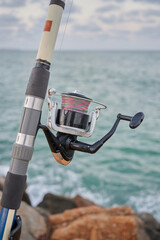 Close up view of a fishing rod and its reel of line placed on the breakwater waiting for the fish...