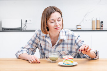Close-up portrait of attractive girl drinking hot matcha tea and eating tasty cake in the kitchen