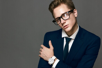 Elegant young handsome man with a wristwatch and glass glasses. Fashion portrait studio.
