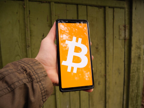Bitcoin symbol displayed on a smartphone screen. BTC is a crypto coin from the world of cryptocurrency. Green wooded forest house with nature in the background.