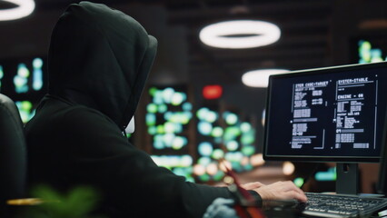 Anonymous hacker breaking data servers at night room closeup. Man looking camera