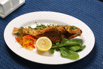 fish whole deep fry flour covered garnished with Arab vegetable white plate blue table 