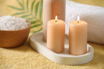 Spa composition. Burning candles, sea salt and towel on soft yellow fabric