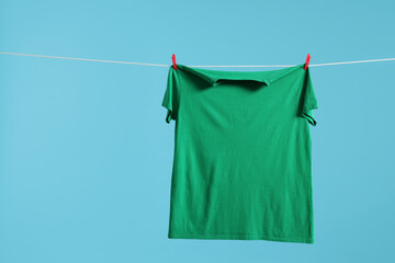 One green t-shirt drying on washing line against light blue background. Space for text